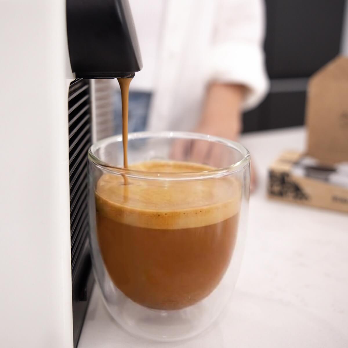 Urban Brew pod brewing in a Nespresso machine, pouring rich crema into a double-walled glass