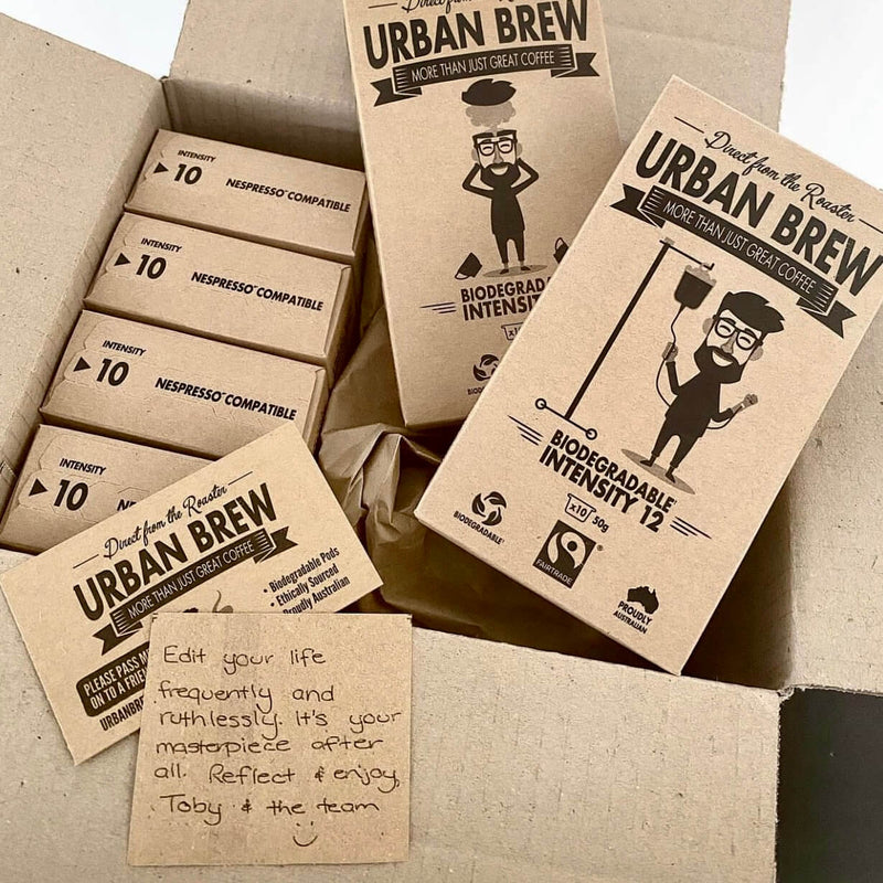 A collection of biodegradable cardboard boxes for coffee bags, labeled 'URBAN BREW' and 'Toby Bag', arranged inside a larger open cardboard shipping box with a handwritten note.