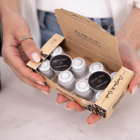 A person holds an open kraft paper box containing multiple small coffee pods. The box is branded 'Coffee at the Table' and 'Café Artisanal', with two pods showing black lids labeled 'Line Stout (Coffee)'.